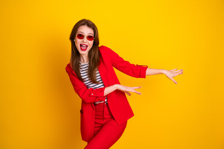 Young woman in a stylish red suit posing against a vibrant yellow background with a cheerful and lively expressionの写真素材