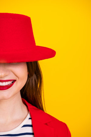 Charming woman in red hat and jacket smiling in front of yellow background showcasing trendy styleの写真素材
