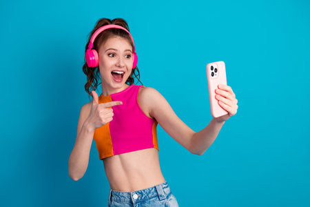 Young woman enjoying music and taking a selfie with a phone against a vibrant blue background