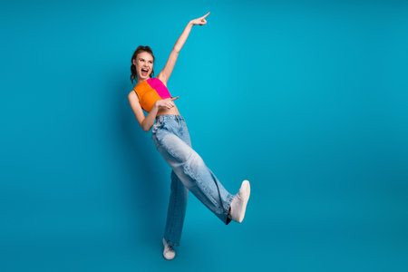 Cheerful young woman in vibrant top and jeans enjoying an energetic moment against a vibrant blue backdropの写真素材
