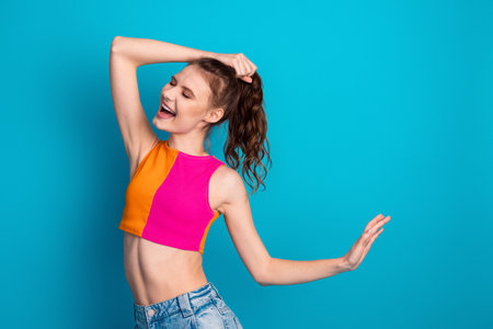 Young woman in vibrant outfit enjoying and posing against bright blue background showcasing trendy...