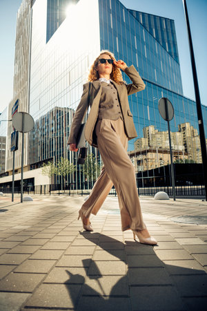 Confident businesswoman walking outdoors with a formal suit in an urban environment on a sunny dayの写真素材