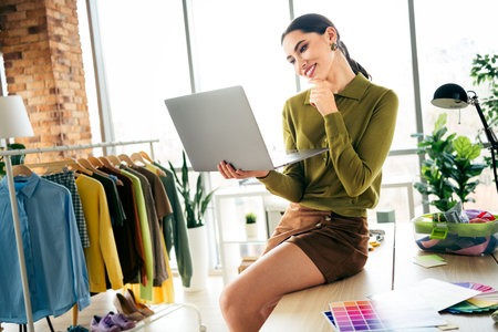 Young businesswoman working in a bright, modern fashion studio with apparel items and fabrics, exuding creativity and focusの写真素材