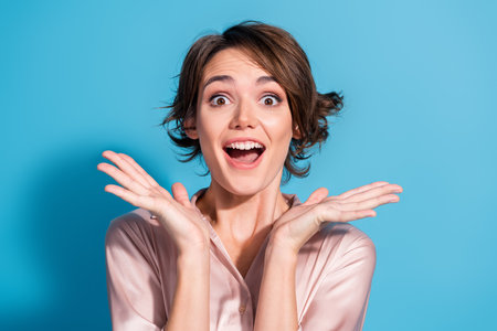 Joyful young woman in satin blouse expressing happiness against a vibrant blue backgroundの写真素材