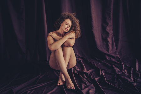 Natural beauty in a studio setting featuring a young woman embracing self-care and body positivity against a rich purple textile backdropの写真素材