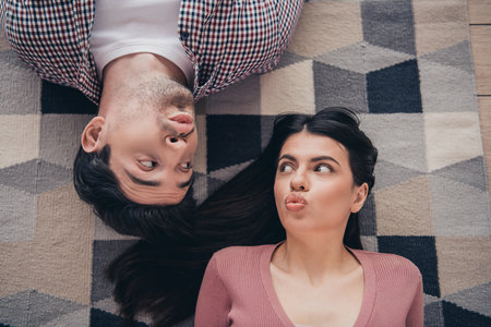 Young couple playfully lying on a patterned rug at home, expressing fun and bonding moments with cheerful expressionsの写真素材