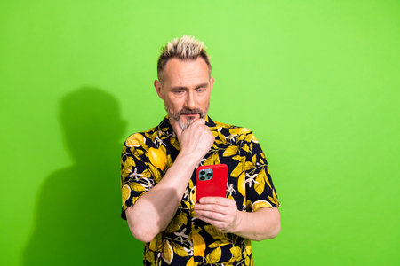 Mature man with trendy summer shirt viewing smartphone against a vibrant green backdrop