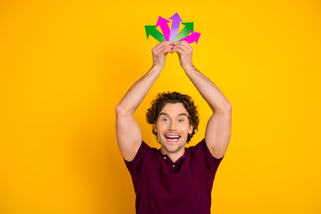 Cheerful Young Man Posing with Colorful Arrows Representing Success on a Bright Yellow Background