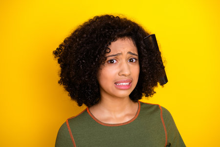Young woman with curly hair and a comb showing a perplexed expression against a bright yellow...