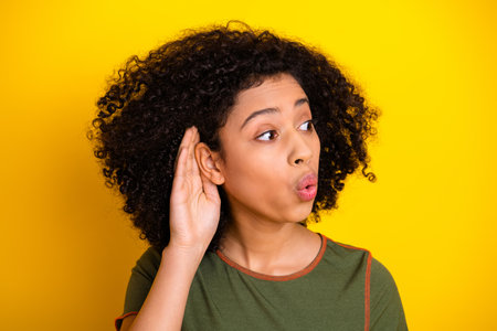 Young woman listening attentively with a curious expression against a vibrant yellow background in...