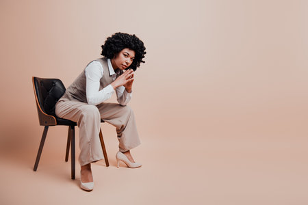 Confident businesswoman sitting on a chair with a pensive gesture wearing formal attire against a neutral backgroundの写真素材
