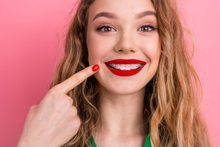 Stylish young woman with braces on pink background showing a joyful expression and sporting vibrant cosmetics.の写真素材