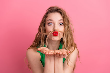 Young woman with playful expression and red lips in front of pink background, posing with a quirky hand gestureの写真素材