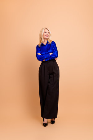 Charming mature woman in trendy business attire posing confidently on beige background for professional eleganceの写真素材