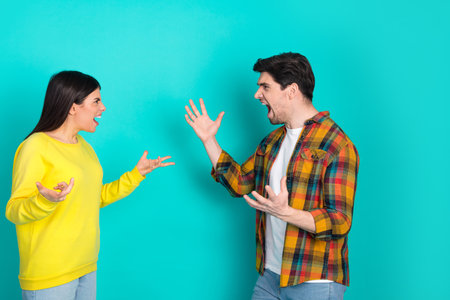 Two young people expressing emotions with hand gestures against a turquoise background capturing lively interactionの写真素材