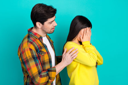 Young man comforting upset woman with hands on her face against teal background expressing empathy...