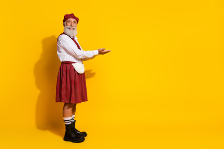Mature Man in Traditional Scottish Attire Gesturing on Yellow Background for Culture and Style Promotionの写真素材