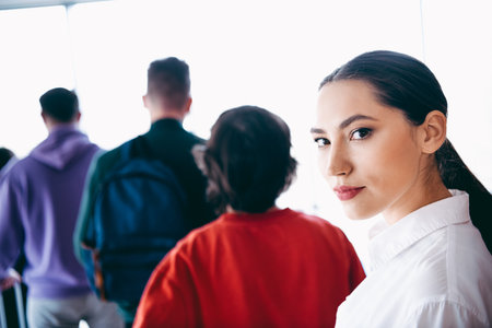 Confident young woman at an airport departure gate surrounded by travelers, expressing style and...
