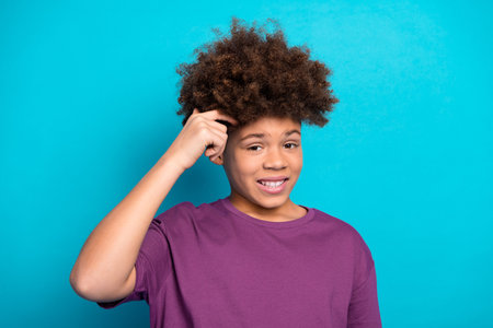 Charming young boy with curly hair posing confidently against a vibrant blue background in casual purple outfitの写真素材