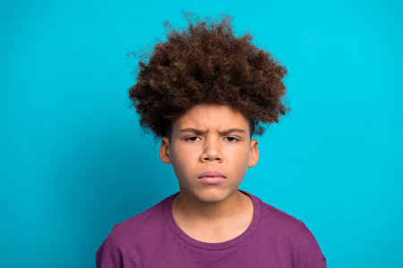 Expressive boy with a stylish hairstyle poses against a vibrant blue background, wearing a purple t-shirtの写真素材