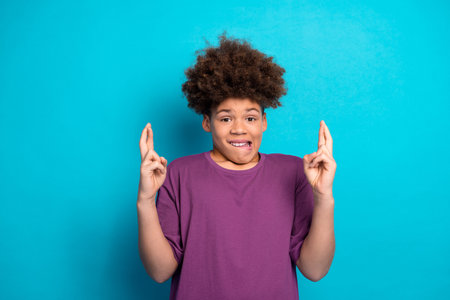 Charming young boy crossing fingers with a playful expression on a blue background. Stylish kid posing casuallyの写真素材