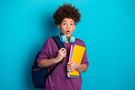 Teenage boy wearing headphones and holding notebooks with a surprised expression against a vibrant...
