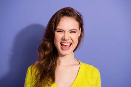 Beautiful young woman in yellow sweater smiling playfully against a purple background, expressing...