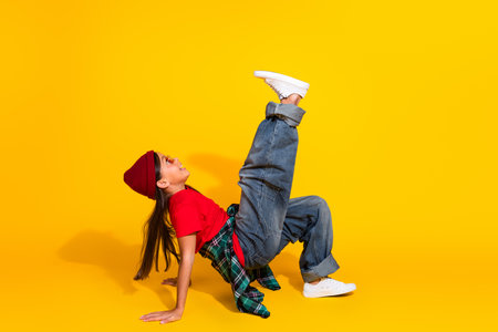 Stylish young girl doing dynamic dance pose against vibrant yellow background showcasing trendy and lively fashion styleの写真素材
