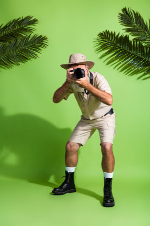 Photo of adventurer senior man focus digital camera photographing in tropics isolated green color backgroundの写真素材