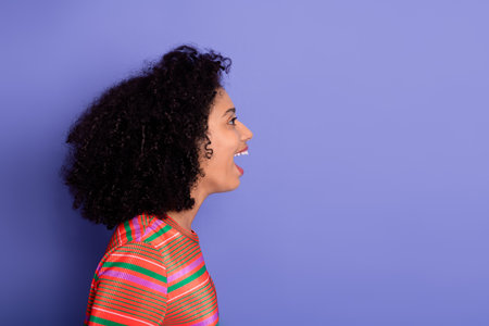 Side profile of a young smiling woman in vibrant striped shirt over purple backgroundの写真素材