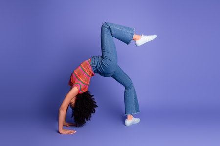 Young woman performs a backbend against a vibrant purple background showcasing flexibility and...