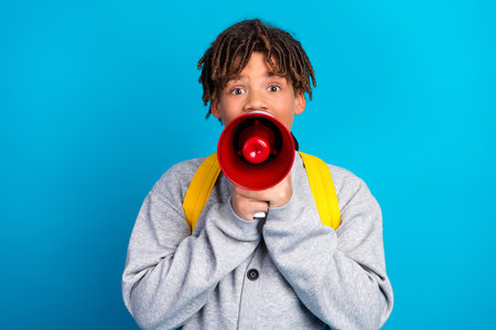 Charming student holding red megaphone with bright expression in front of blue background wearing casual grey cardiganの写真素材