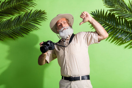Photo of senior adventurer man hold photo camera point finger myself wear safari suit isolated green color backgroundの写真素材