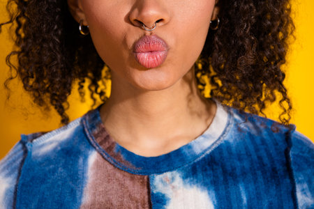 Portrait of a stylish young woman with curly hair wearing casual attire on a vibrant yellow background, exuding charmの写真素材