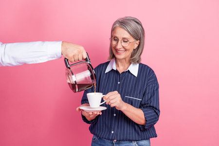 Mature professional woman enjoying coffee with cheerful expression against vibrant pink background symbolizing leisureの写真素材