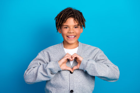 Smiling young boy making a heart gesture on bright blue background expressing love and positivity