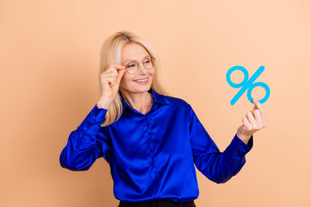 Professional Businesswoman Holding a Percentage Symbol Against a Beige Background While Expressing...