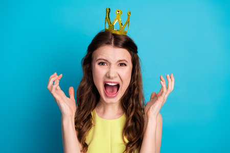 Charming woman wearing yellow dress and crown posing joyfully against a vibrant blue background in a cheerful momentの写真素材