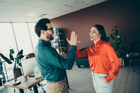 Professional colleagues sharing a highfive gesture in a modern office setting, promoting teamwork,...