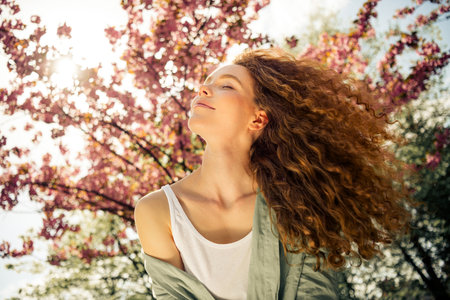 Young woman enjoying a sunny day outdoors with vibrant cherry blossoms in spring, radiating joy and relaxationの写真素材