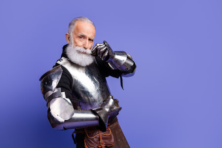 Elderly man in medieval steel armor posing confidently against a vibrant violet backgroundの写真素材
