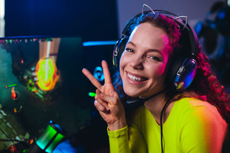 Female gamer wearing headphones enjoying an online gaming session at home surrounded by neon lights