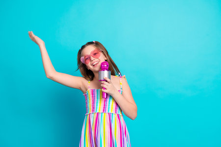 Cheerful young girl holding a heart-shaped microphone, dressed in a colorful striped summer outfit,...