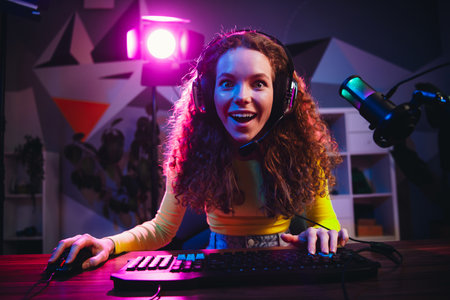 Excited female streamer gaming with colorful neon lighting in a modern home studio at night creating engaging online contentの写真素材