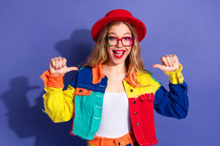 Happy young woman in vibrant colorful outfit posing cheerfully against a purple background,...