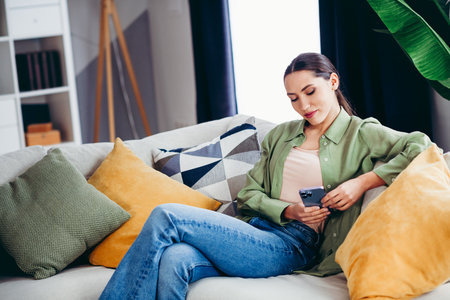 Lovely woman relaxing on sofa at home, scrolling her smartphone while enjoying the cozy atmosphere of her stylish interiorの写真素材