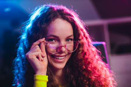 Young female gamer enjoying a casual evening with neon light ambiance, smiling confidently while...