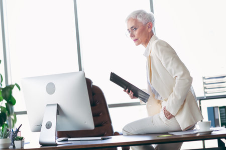 Confident mature professional in elegant suit working in modern office environment with computer and documentsの写真素材