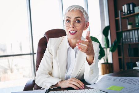 Confident senior businesswoman in formal attire having a professional discussion in a modern office settingの写真素材