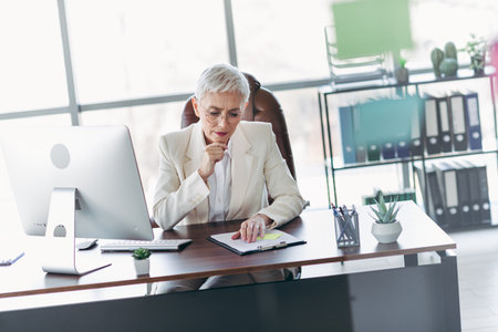 Mature professional businesswoman focused on paperwork at a modern office workspace with formal and elegant appearanceの写真素材